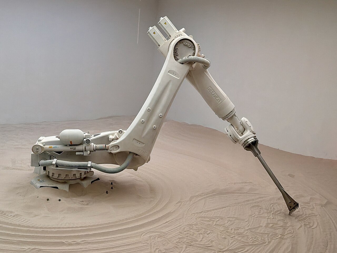 A six-axis KUKA industrial robot arm drawing patterns in sand